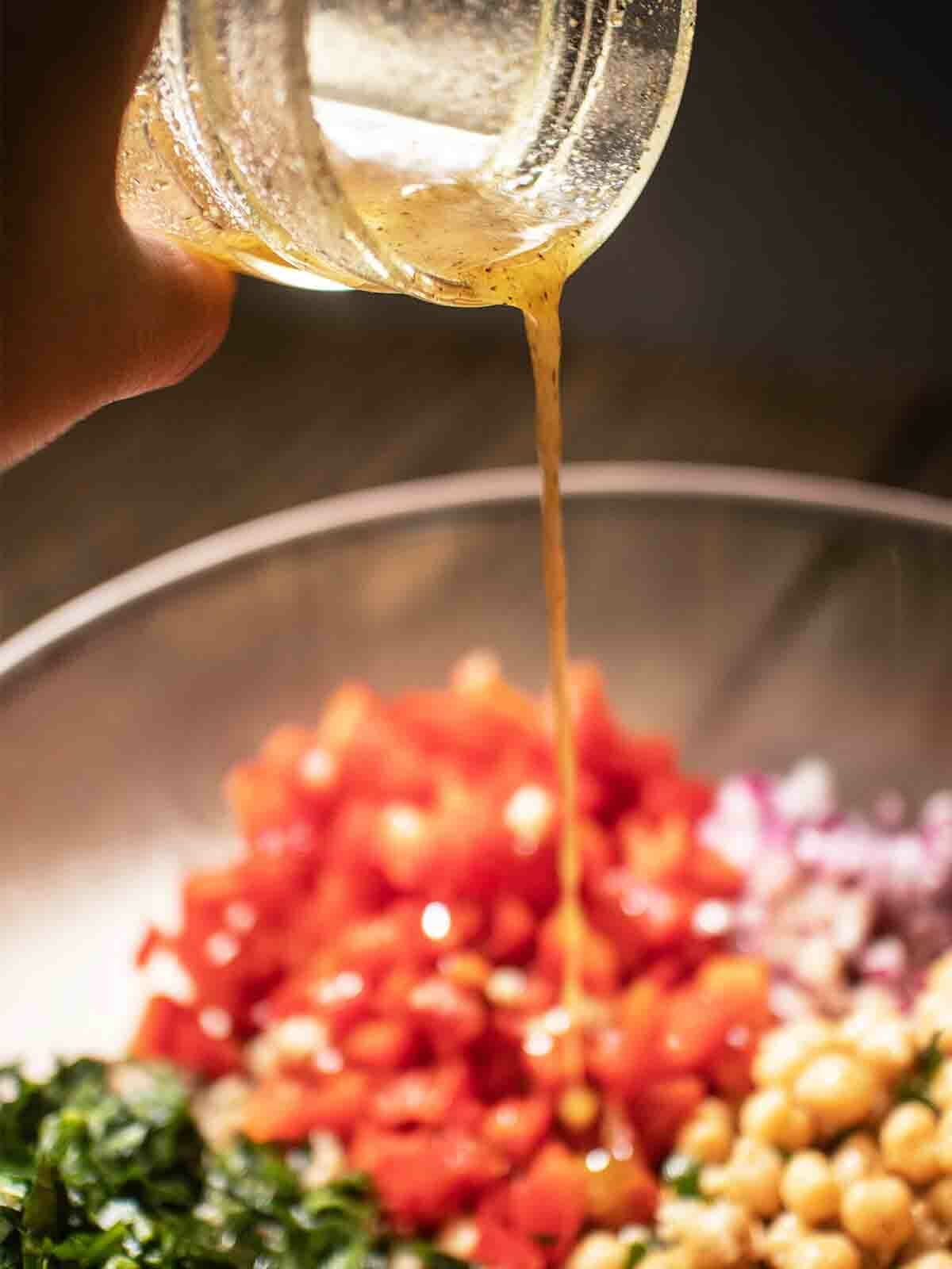 pour cumin salad dressing into ingredients for chickpea-quinoa-salad